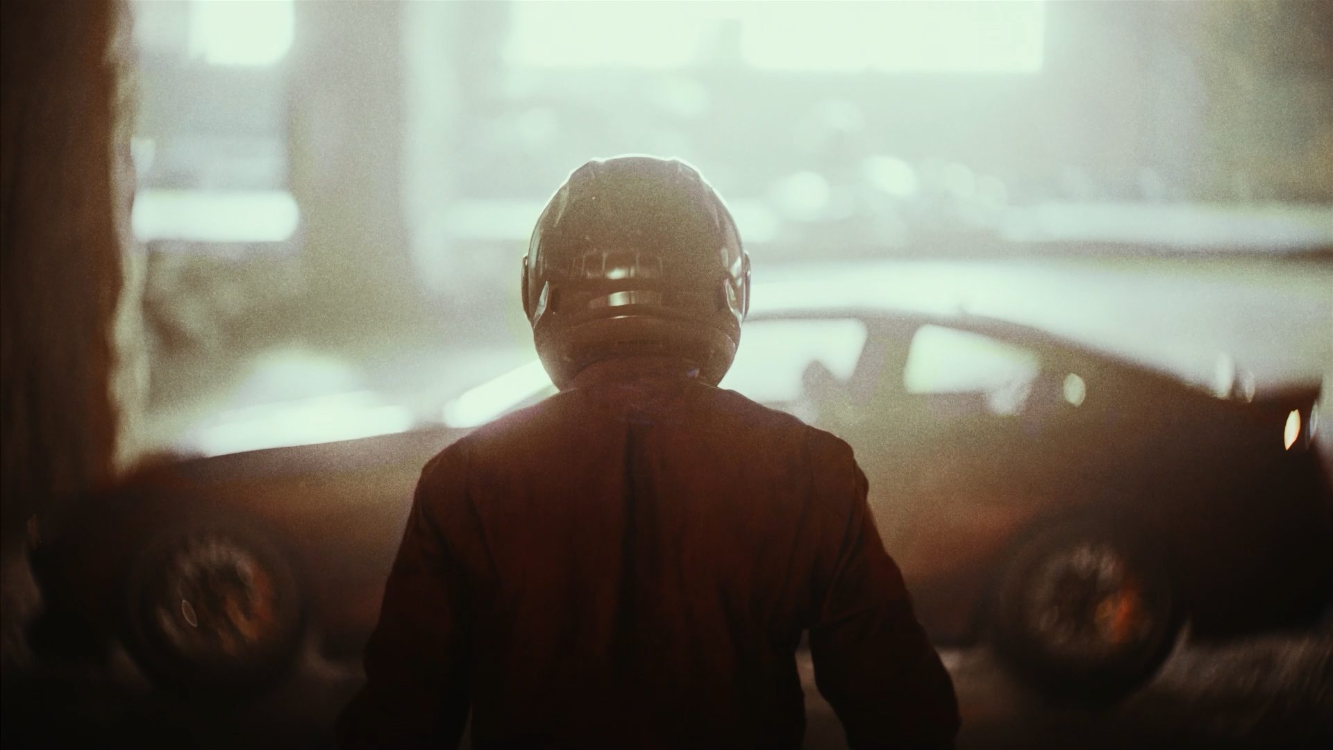 Helmeted figure standing before the car in a hazy, sunlit garage